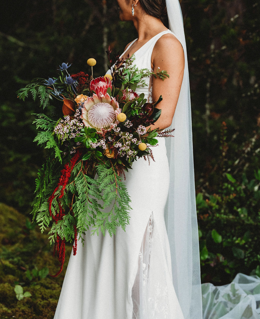 Bride holds west coast bouquet with ferns and protea