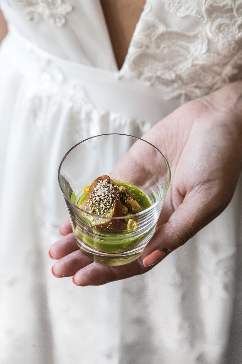 Oyster appetizer in glass held by bride in Park and Fifth Co lace overlay gown