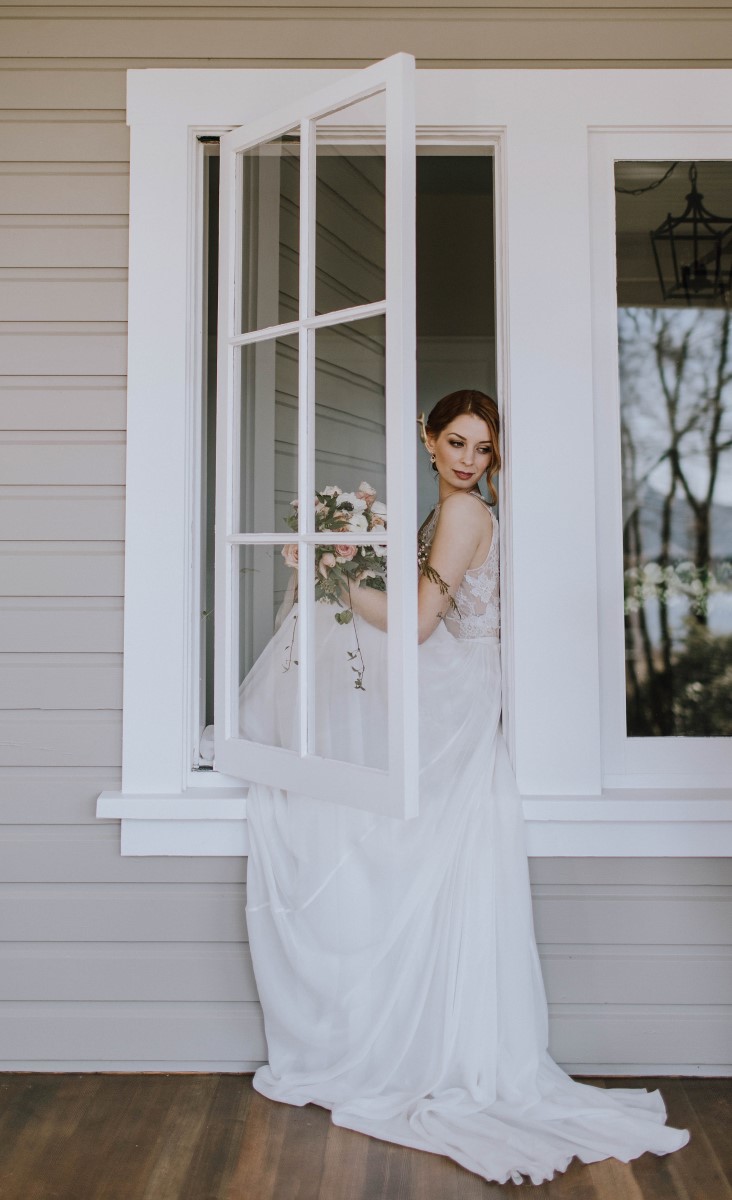 Bride sits on windowsill looking out with dress flowing out the window