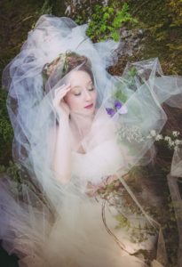 Whimsical Woodland Bride covered with veiling lies in the Vancouver forest