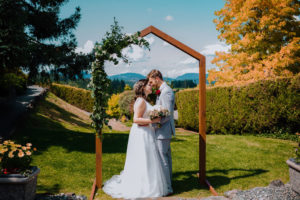 Happily Ever After newlyweds framed by arch with floral design and mountains on Vancouver Island