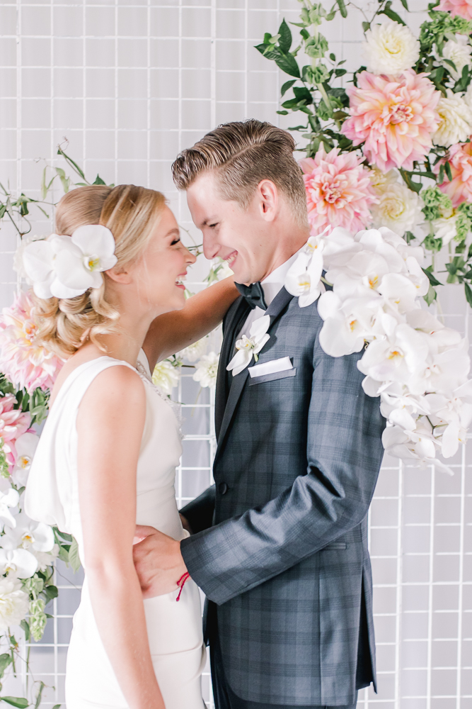 Newlyweds laugh as bride holds white orchid bouquet by Ivy May Floral in Vancouver