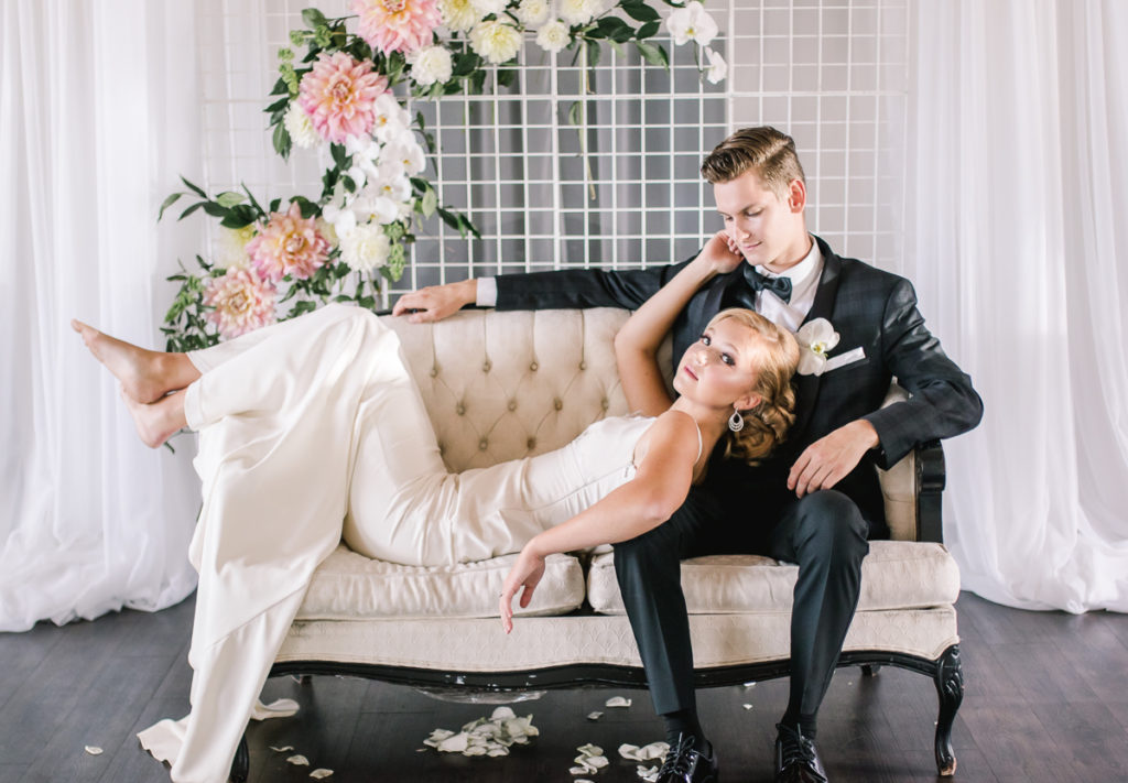 Bride lays her head on groom as they sit on white vintage couch