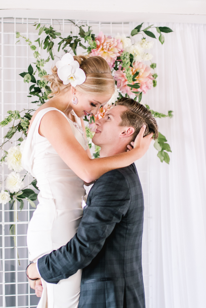 Groom in grey plaid suit holds bride with white orchid in her hair