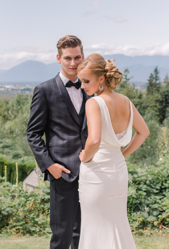 Newlyweds showcase mountain scenery wearing black tie tuxedo and Grecian white wedding gown