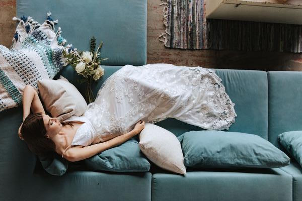 Bride in custom white gown lies on blue couch