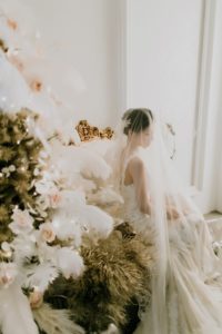 West Coast Weddings Magazine bride indoors next to pine tree decorated with feathers and pink flowers
