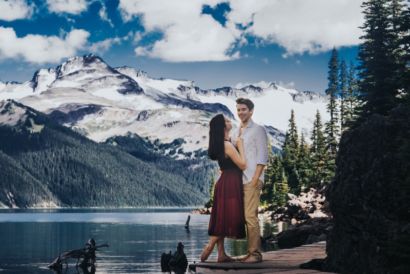 Naturally Romantic Engagement Bride and Groom pose in front of lake and mountains in British Columbia