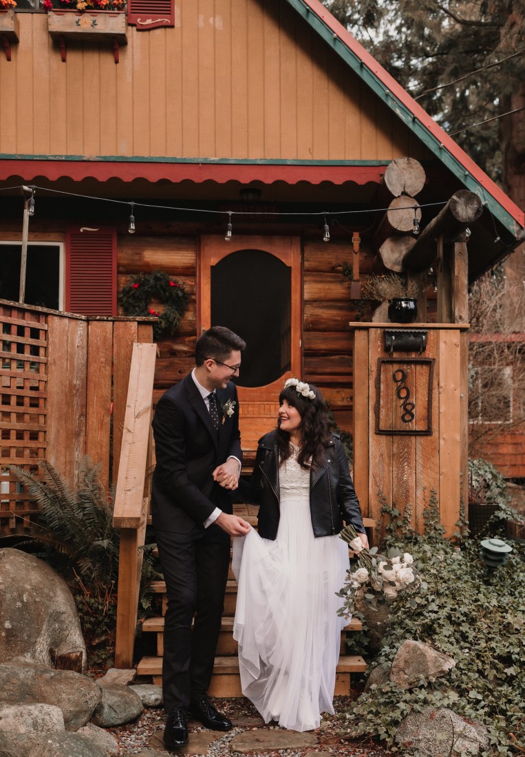 Bride and groom sit on the stairs of a rustic cabin by Coastal Weddings and Events