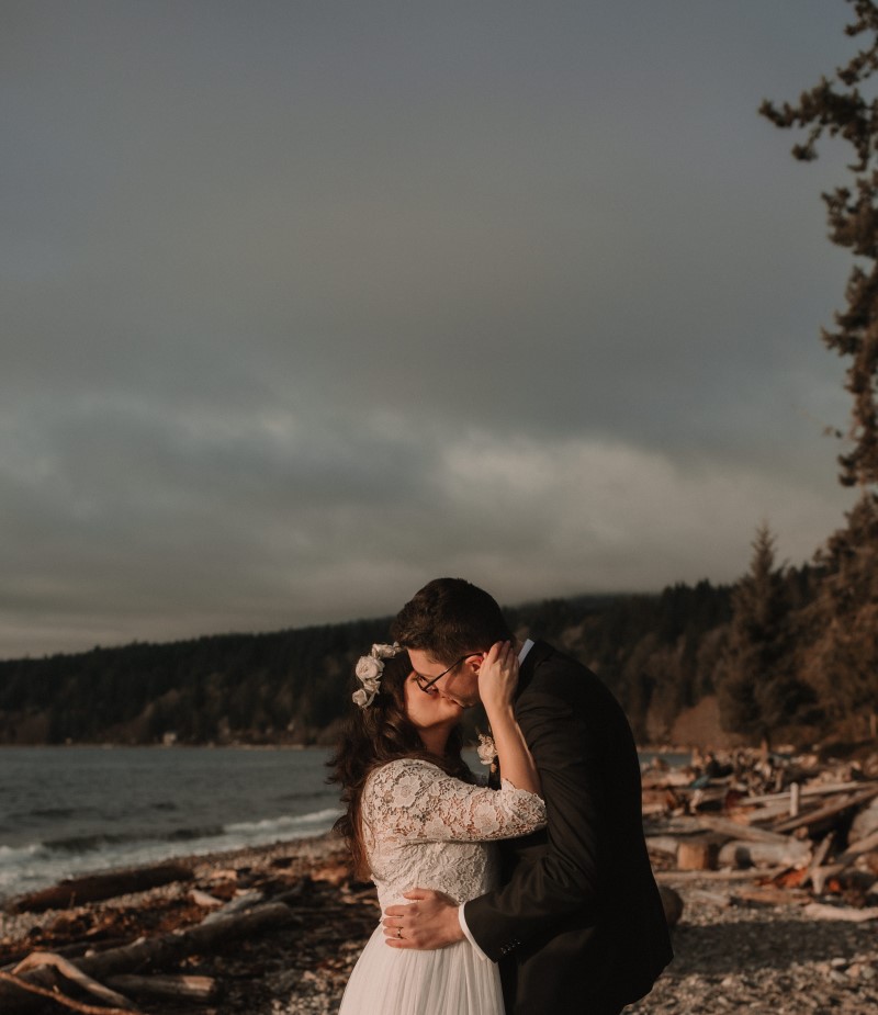 Newlyweds embrace after wedding ceremony on beach filled with logs