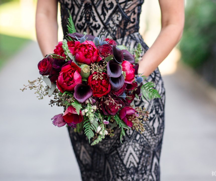Bridal bouquet of red and pink peonies, blue thistle and black calla lily against black lace wedding gown by Thrifty Foods and The Brides Closet