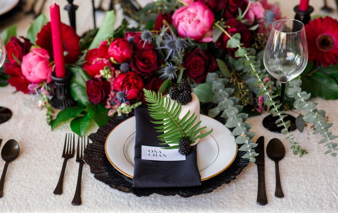 Pink peonies, eucalyptus and fern on black plates on wedding reception table by Thrifty Foods