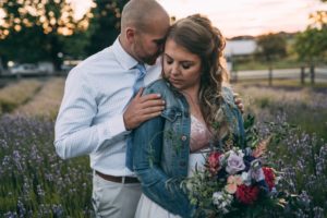 Bride in jean jacket holding bouquet and groom wearing white shirt