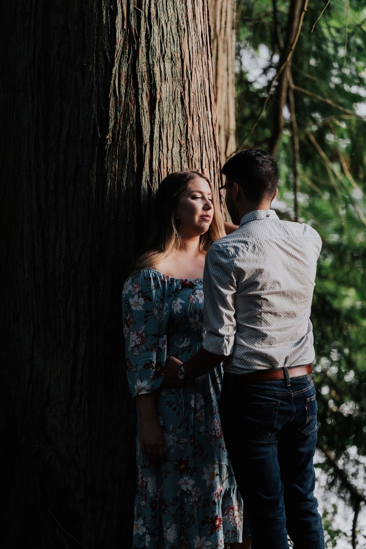 Engaged Romance couple stand against tree smiling