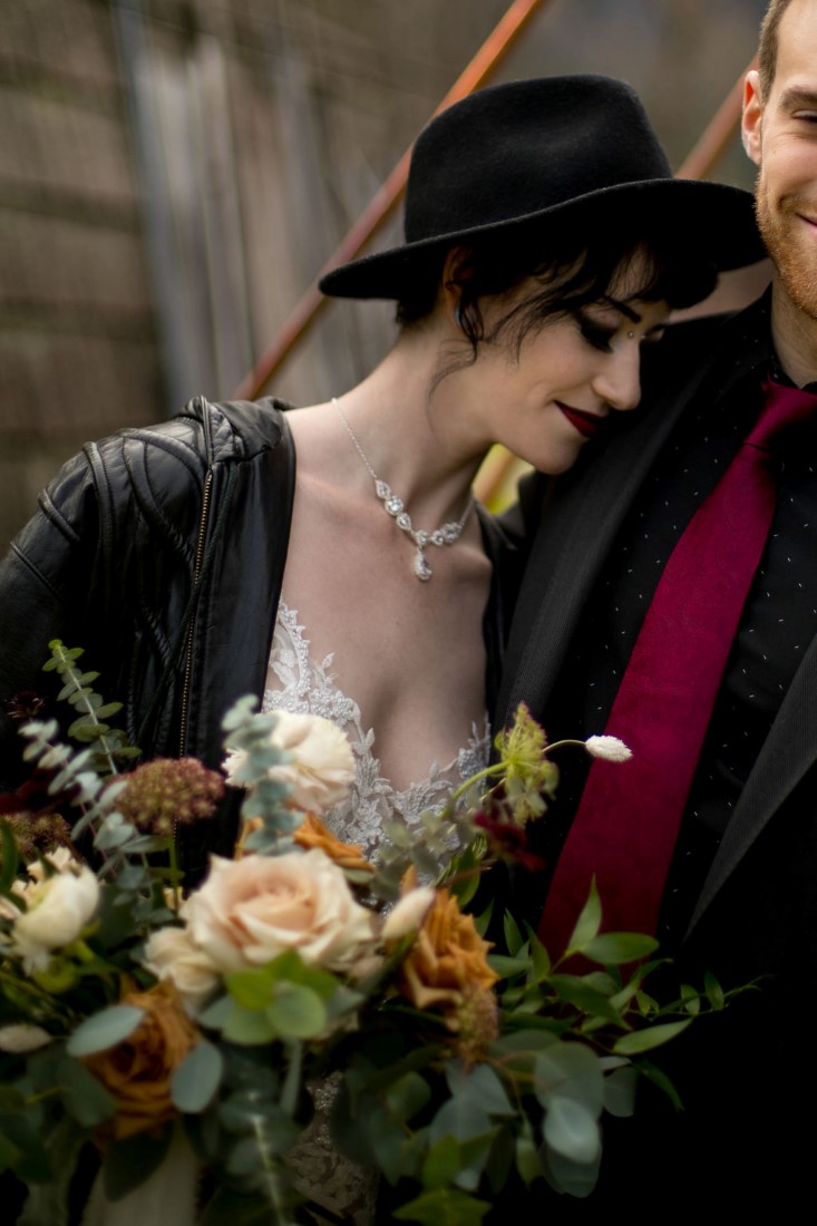 Bride wearing black leather jacket and hat carrying bouquet