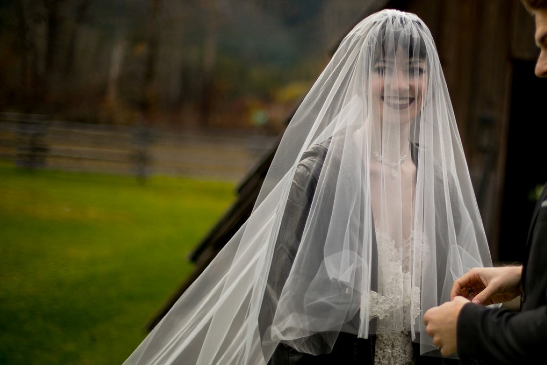 Bride smiles through cathedral veil wearing black leather jacket