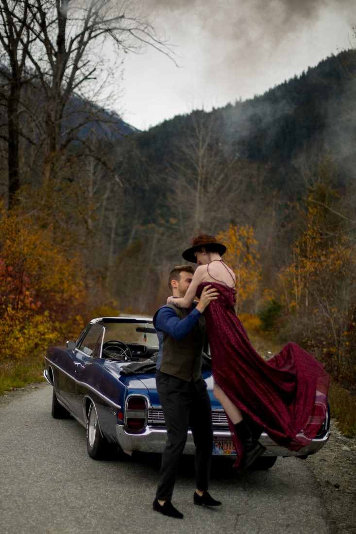 Groom sweeps bride off her feet in front of blue classic car at Vancouver wedding