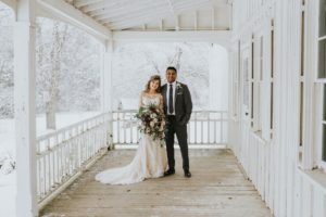 Bride and Groom on Farmhouse porch with snowstorm behind by White Canvas Photo