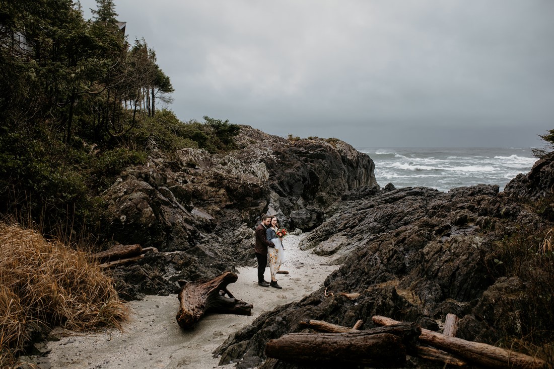 Bride and groom walk through beach rocks at Tofno