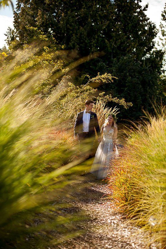 Bride and Groom walk through tall grass at Van Dusen Botanical Gardens
