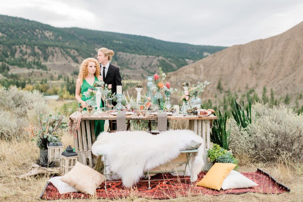 Ciouple stands behind boho tablescape with coloured glass bottles and white fir