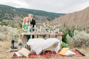 Ciouple stands behind boho tablescape with coloured glass bottles and white fir