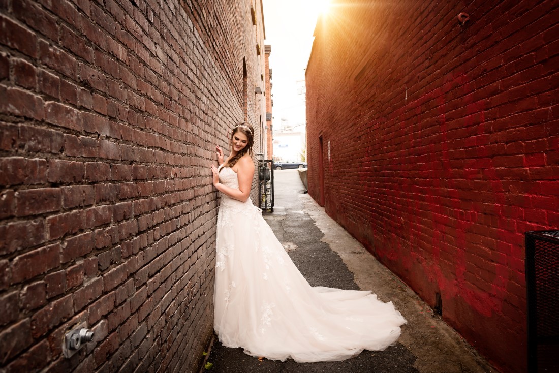 Bride stands in allwy with sunshine behind her