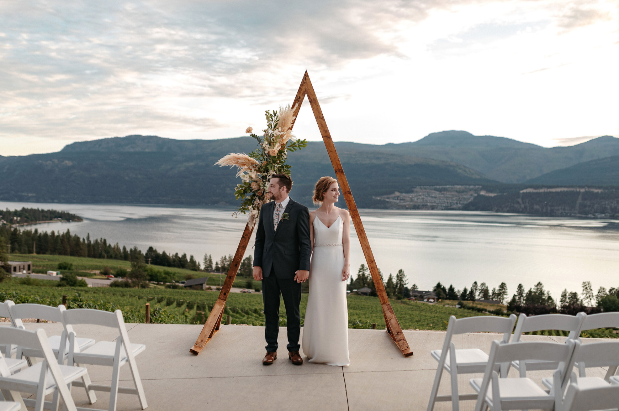 Couple on ceremony deck in front of wedding backdrop and lake in the Okanagan