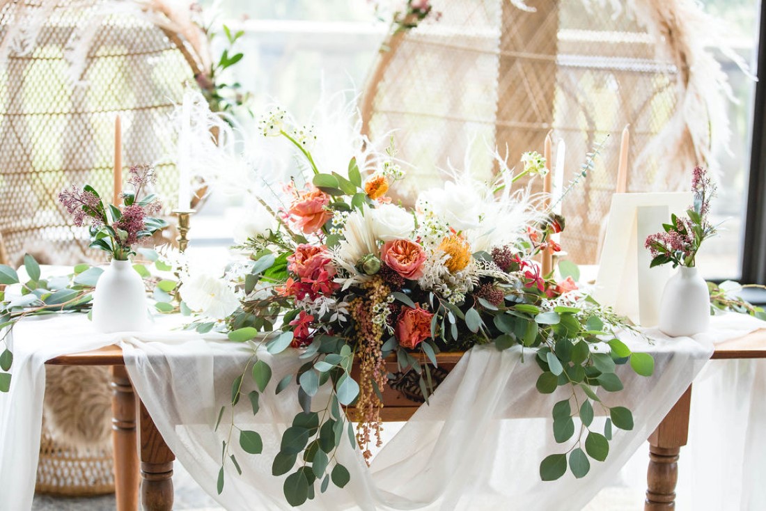 Florals on the front of sweetheart table feature eucalyptus, pampas grass, pink and peach roses by Maple Ridge Floral Ltd