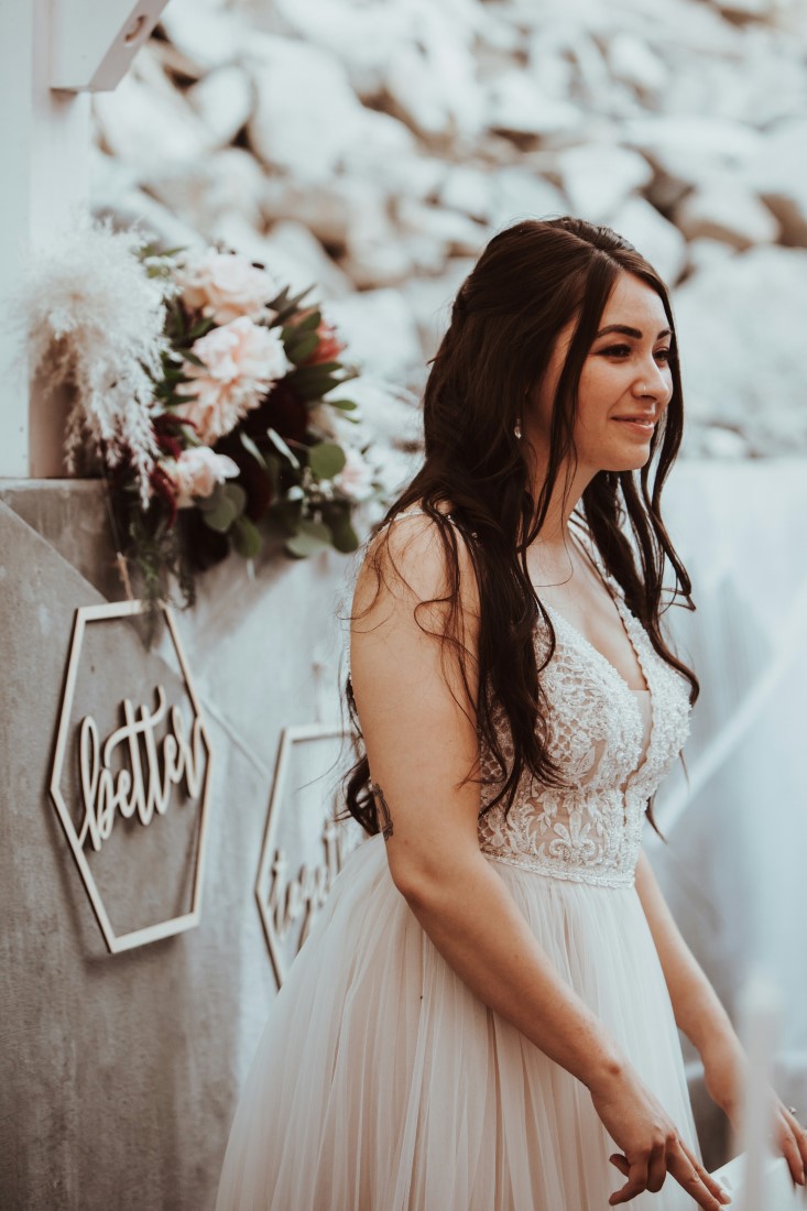 Bride smiles out over her guests with flowers behind her