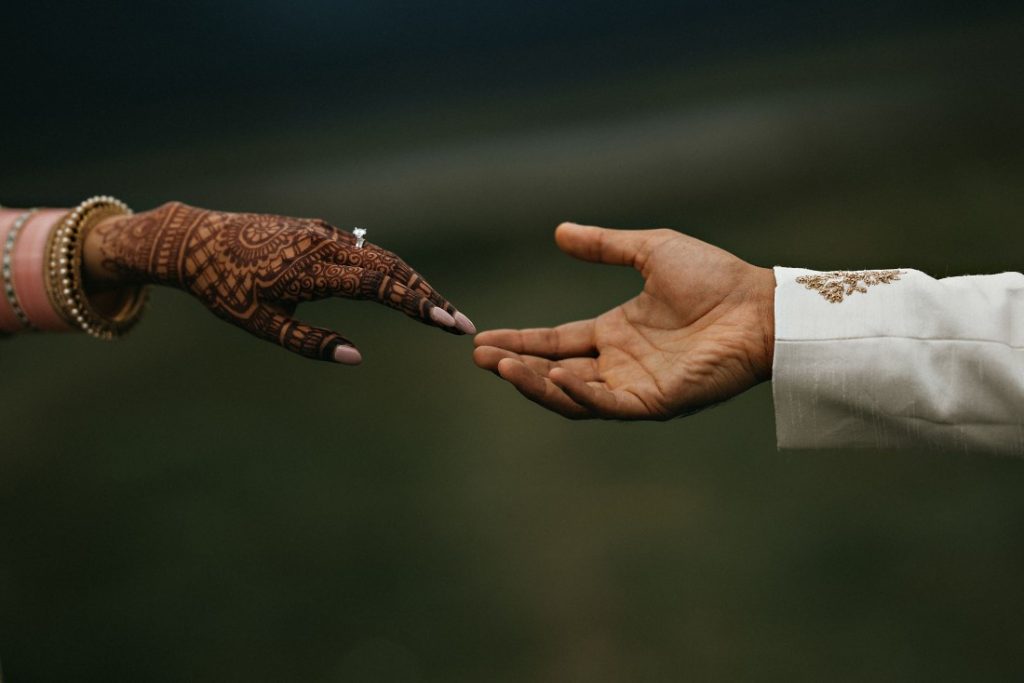 Bride and groom reach for each other's hands by Amrit Photography