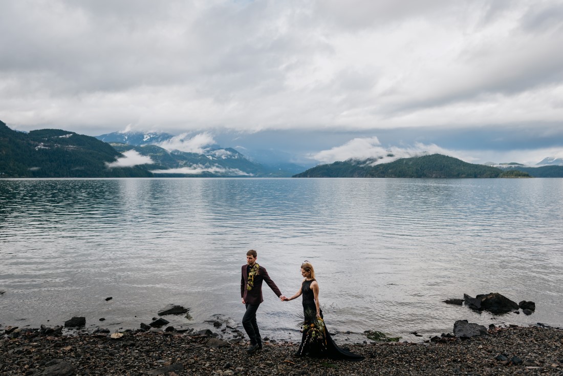 Newlyweds walk in front of Harrison Lake with mountains behind