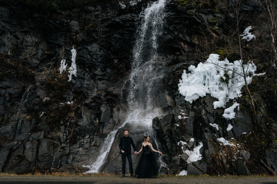 Bride and Groom walk in front of frozen waterfall by Leanne Sims