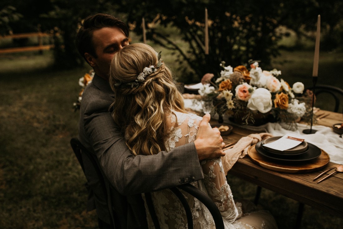 Newlyweds embrace while seated at a farm table at Keating Farm