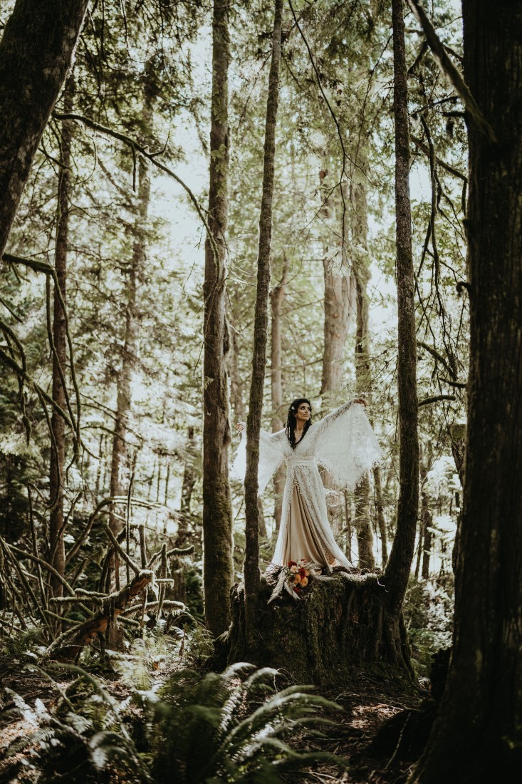 Whimsical & Woodsy bride lifts her lace sleeves while standing on a tree stump