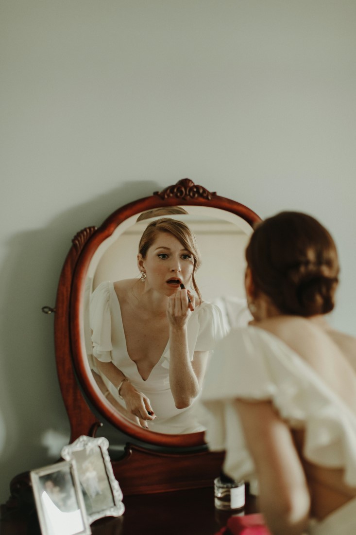Bride puts on lipstick in mirror by Mike and Shari