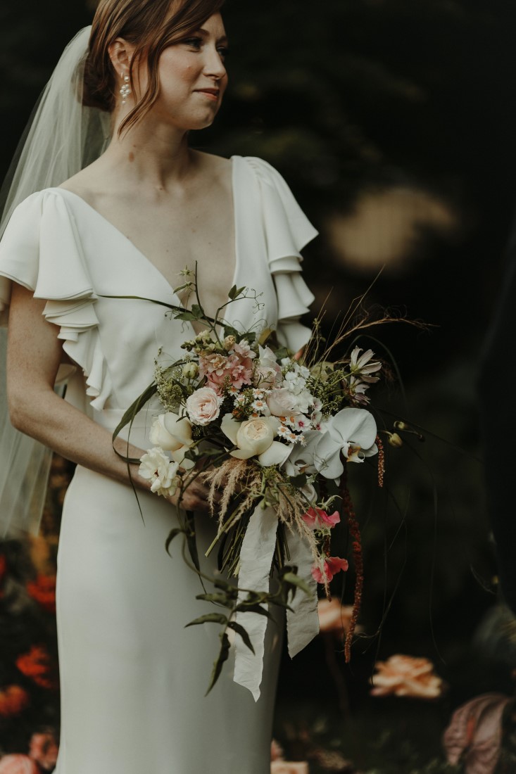Bride holds bouquet of white flowers by The Wild Bunch Vancouver