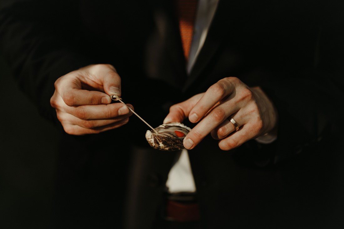 Groom holds oyster on a spoon at Vancouver wedding
