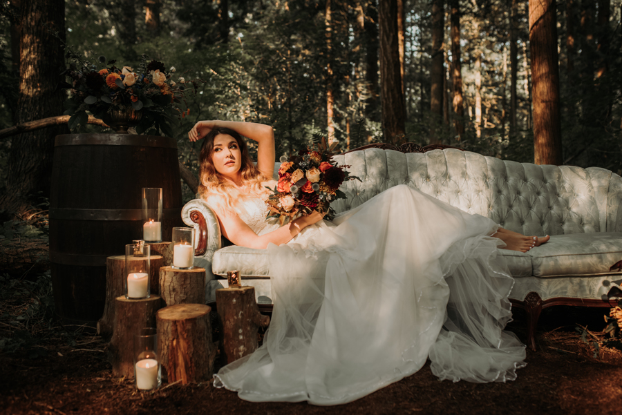 Bride lounges on sun dappled vintage couch in the forest