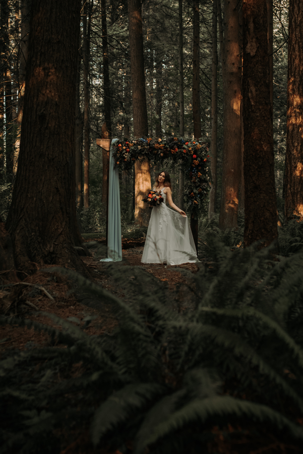 Bride poses beneath wood arch in the forest covered in flowers