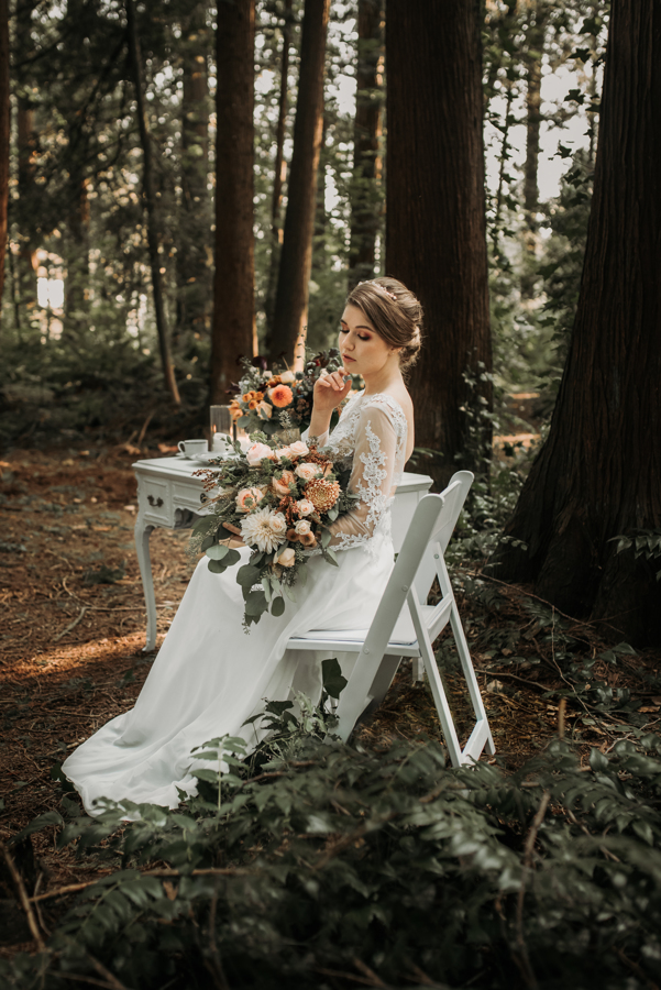 Bride sits at vintage table with blush bridal bouquet