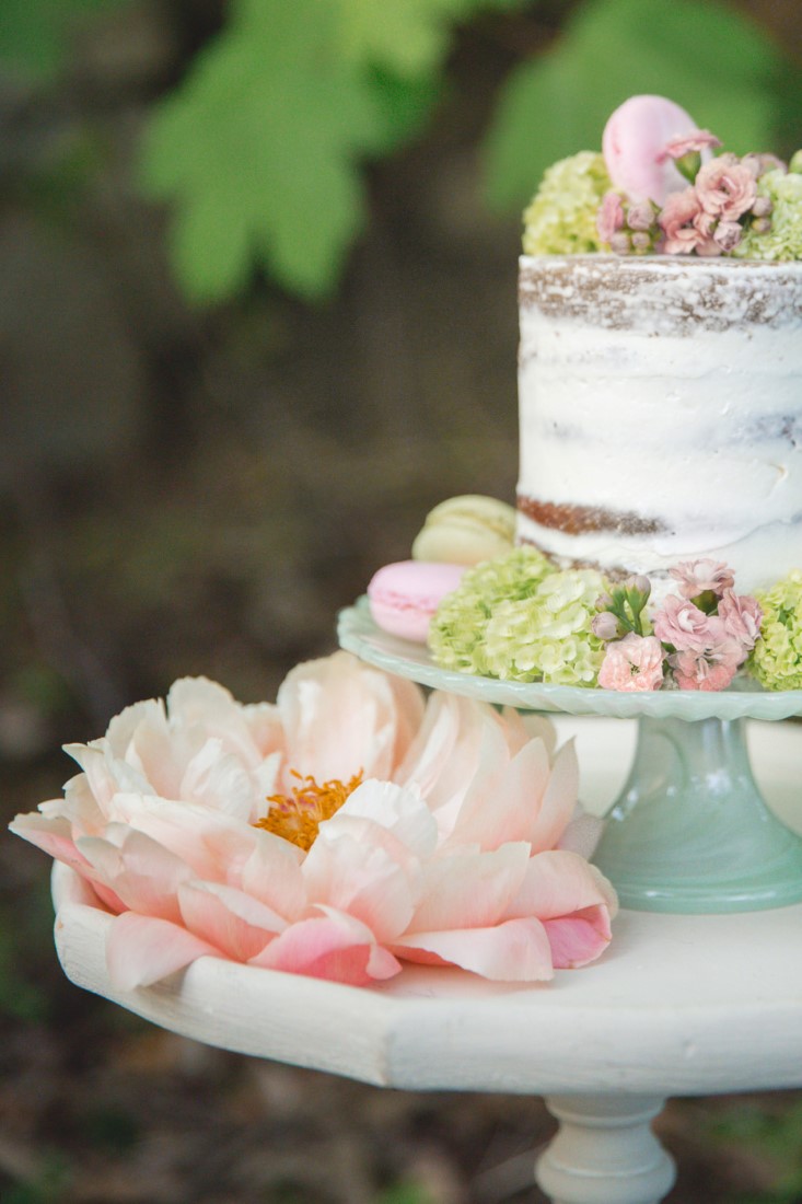 Pink peonies next to white naked wedding cake at garden party