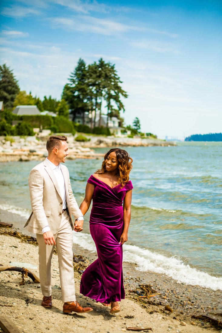 Bride in purple velvet gown and groom in beige linen suit walk along Vancouver beach