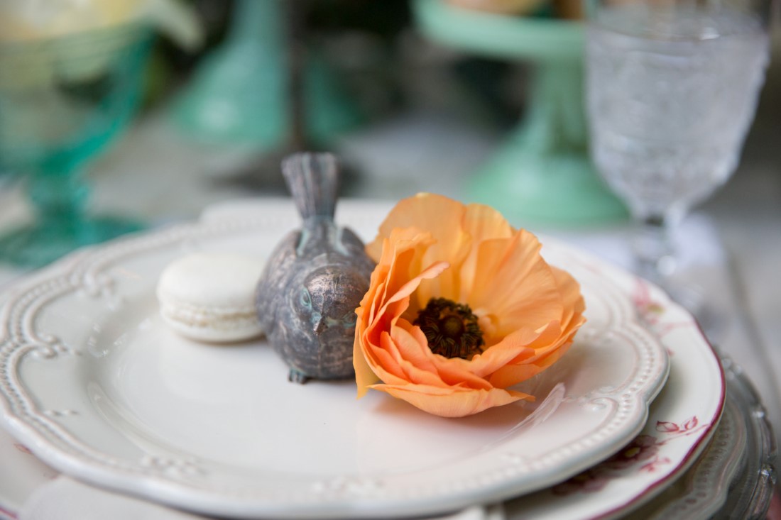Peach flower sits next to grey bird on white wedding reception plate
