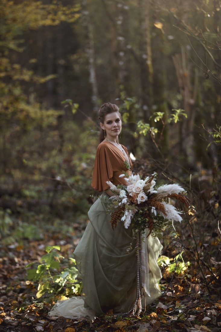 Bride in orange and green gown holds pampas grass bouquet in Vancouver forest
