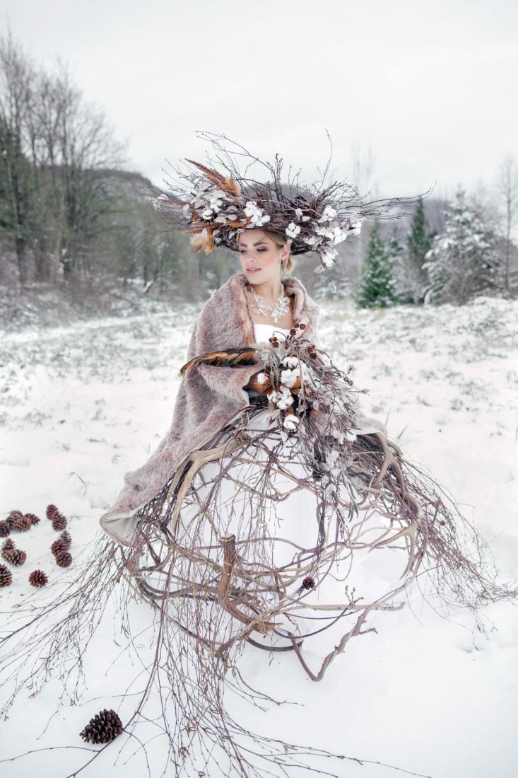 Winter bride with willow wreath sits atop snow with bouquet by Deborah Lee Designs