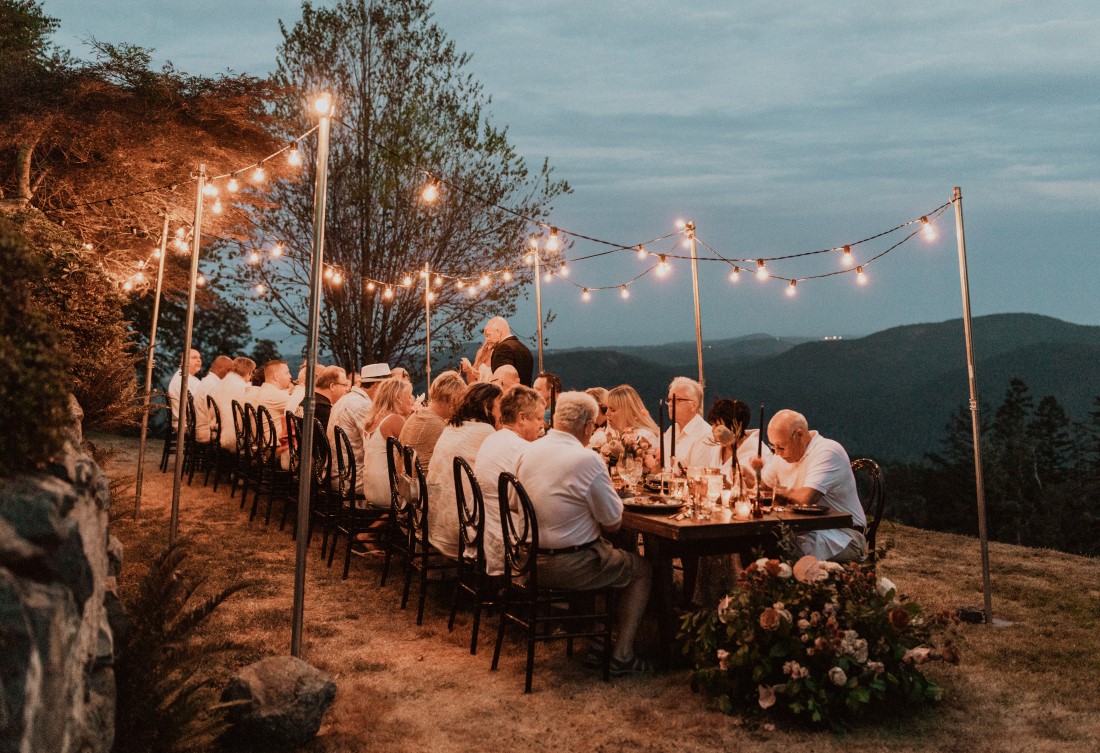 Guests sit in twilight atop a mountain eating wedding supper at Villa Eyrie