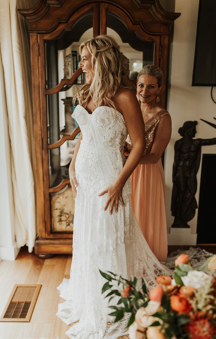 Bridesmaid helps bride put on her wedding gown