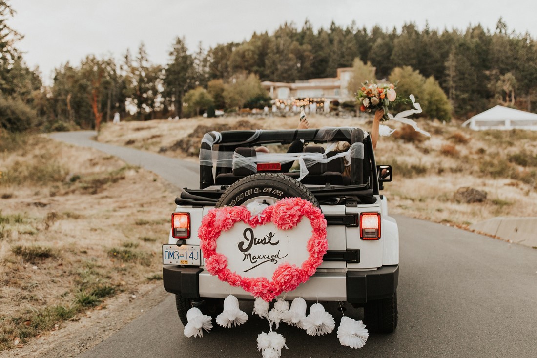 Newlyweds drive away in a Jeep Cherokee with heart on the back
