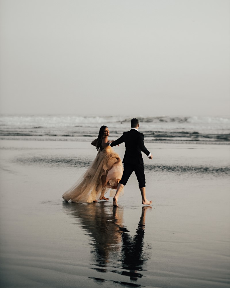 Newlyweds run towards the waves on Tofino beach on Vancouver Island